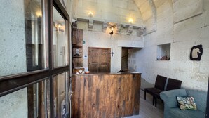 Un interior rústico con un mostrador de recepción de madera, paredes de piedra y una zona de estar acogedora con un sofá estampado.