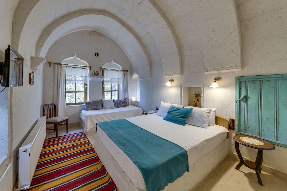 A room with two beds, a radiator, a striped carpet, and a small table.