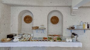 Una mesa con una variedad de alimentos y condimentos en un bufé, frente a una pared texturizada con nichos abovedados.