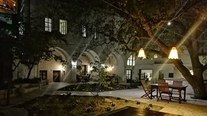 Un patio con una mesa y sillas de madera, rodeado de árboles y un edificio con ventanas de arco.