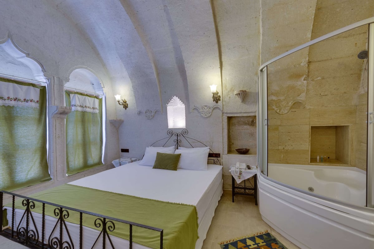 A bedroom with a large bed, a bathtub, and a small table with a telephone.