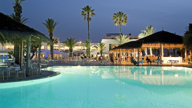 A swimming pool with lounge chairs and umbrellas, surrounded by palm trees and buildings. - Thalassa Sousse Resort & Aquapark (Sousse)