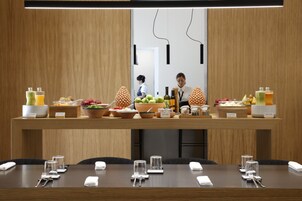 Un ricco buffet per la colazione con diversi cibi e bevande, un membro dello staff che assiste gli ospiti e un tavolo da conferenza apparecchiato con stoviglie e accessori.