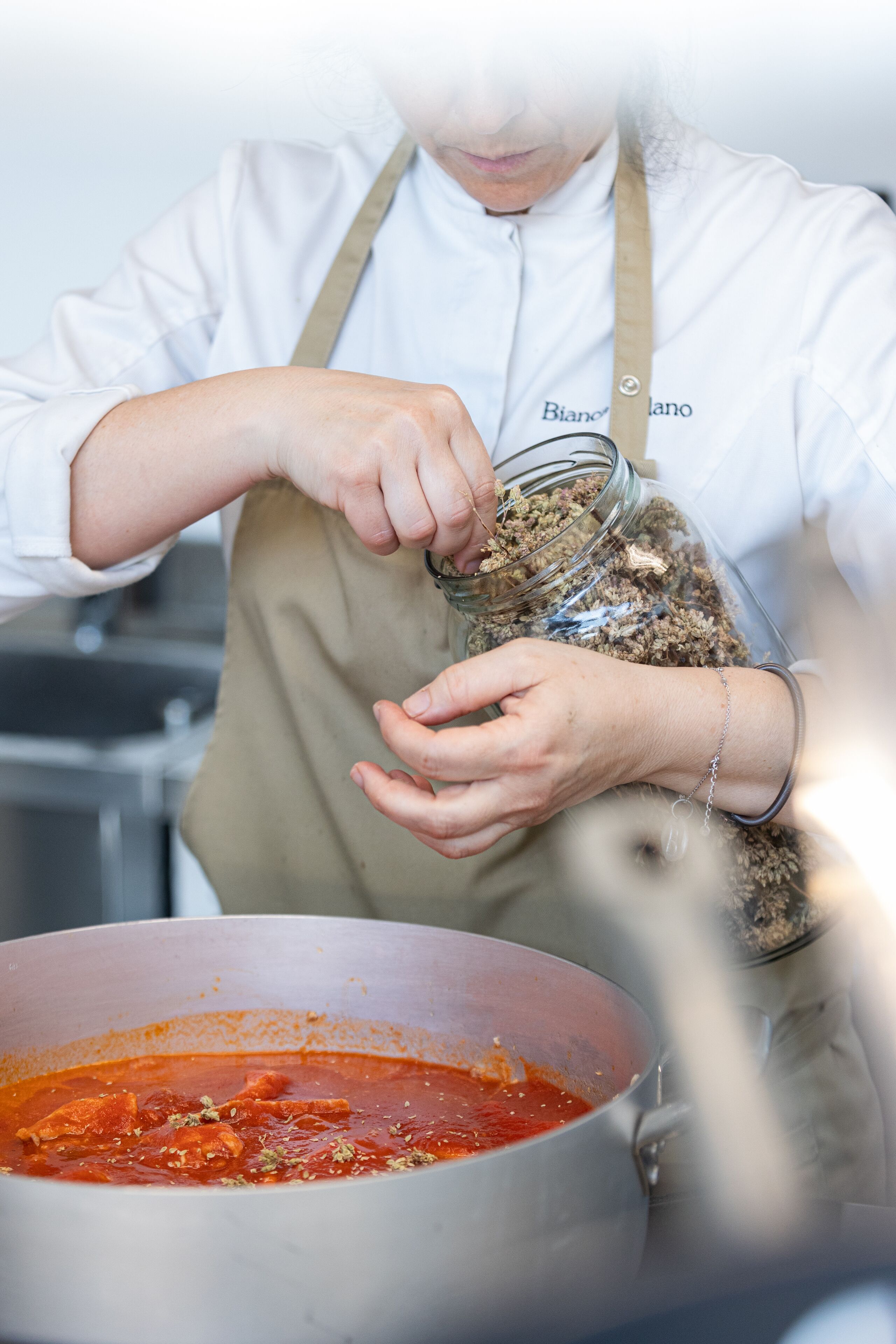 A person in a white chef's coat and apron handling food ingredients.