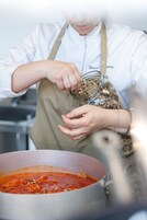 Una persona con uniforme de chef blanco y delantal manipulando ingredientes alimentarios.