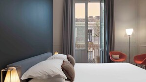 Camera d'albergo con un letto grande, un comodino con una lampada, una sedia e vista sul balcone esterno.