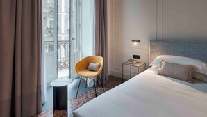 Una camera d'albergo con un letto, una sedia, un comodino e vista sugli edifici.