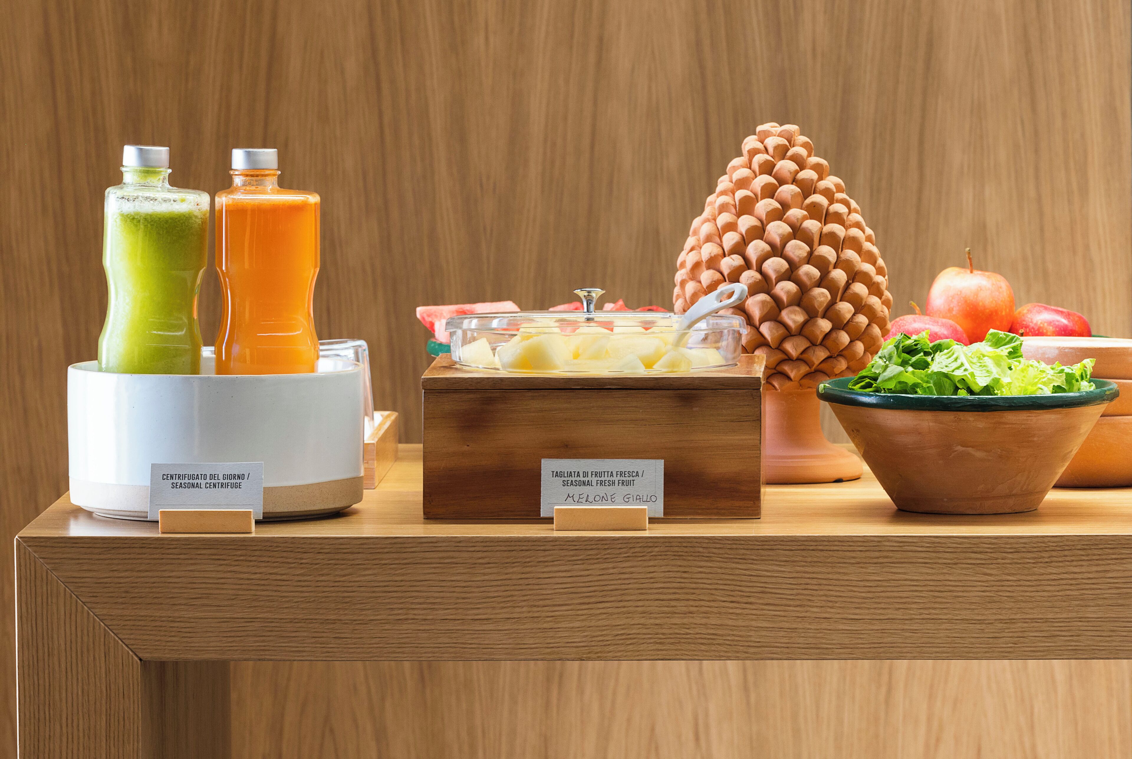 Un buffet de petit-déjeuner avec des fruits frais, un centre de table décoré avec des pommes de pin et un saladier de légumes verts.