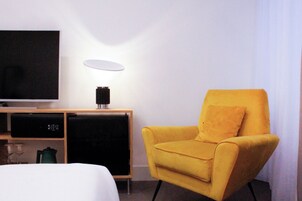 Una habitación de hotel con una cama, televisión, refrigerador pequeño y un sillón amarillo.