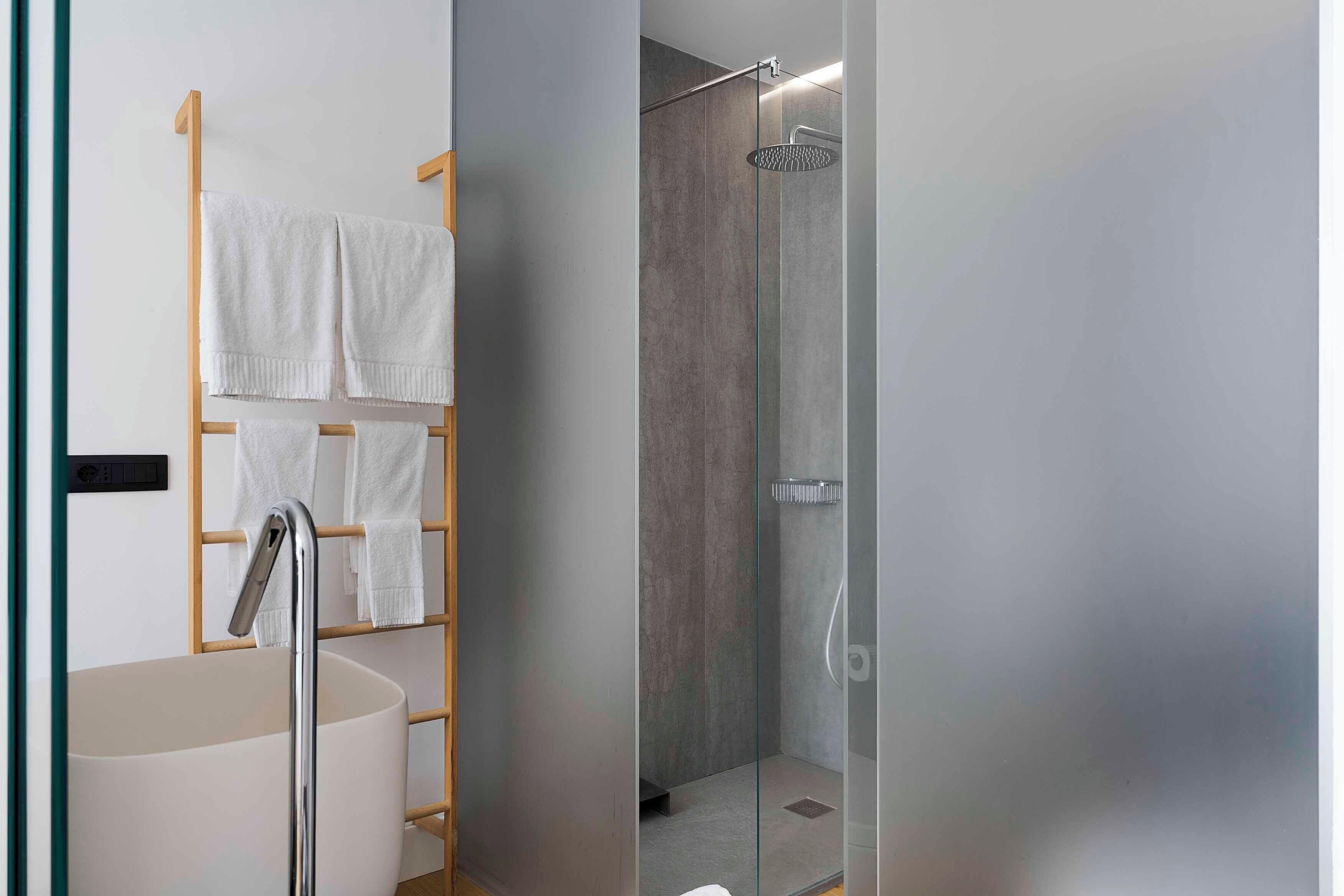 A modern bathroom with a freestanding bathtub, a glass-enclosed shower, and a towel rack with multiple towels.