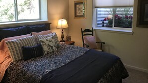Un dormitorio con cama, mesita de noche, silla, ventana con persianas y ventilador de techo.