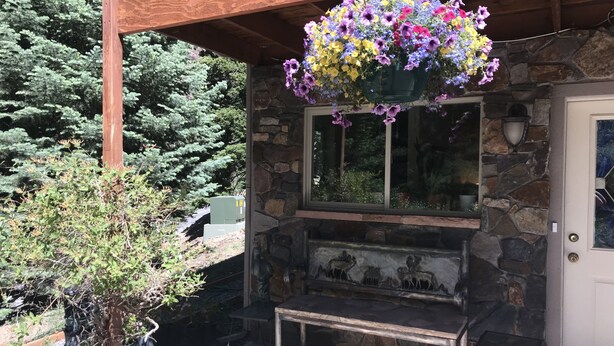 Un edificio de piedra con un porche de madera, una cesta de flores colgante y una chimenea de piedra.