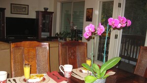 Una mesa de comedor con un jarrón de orquídeas rosadas, un vaso de jugo de naranja y un plato de comida.