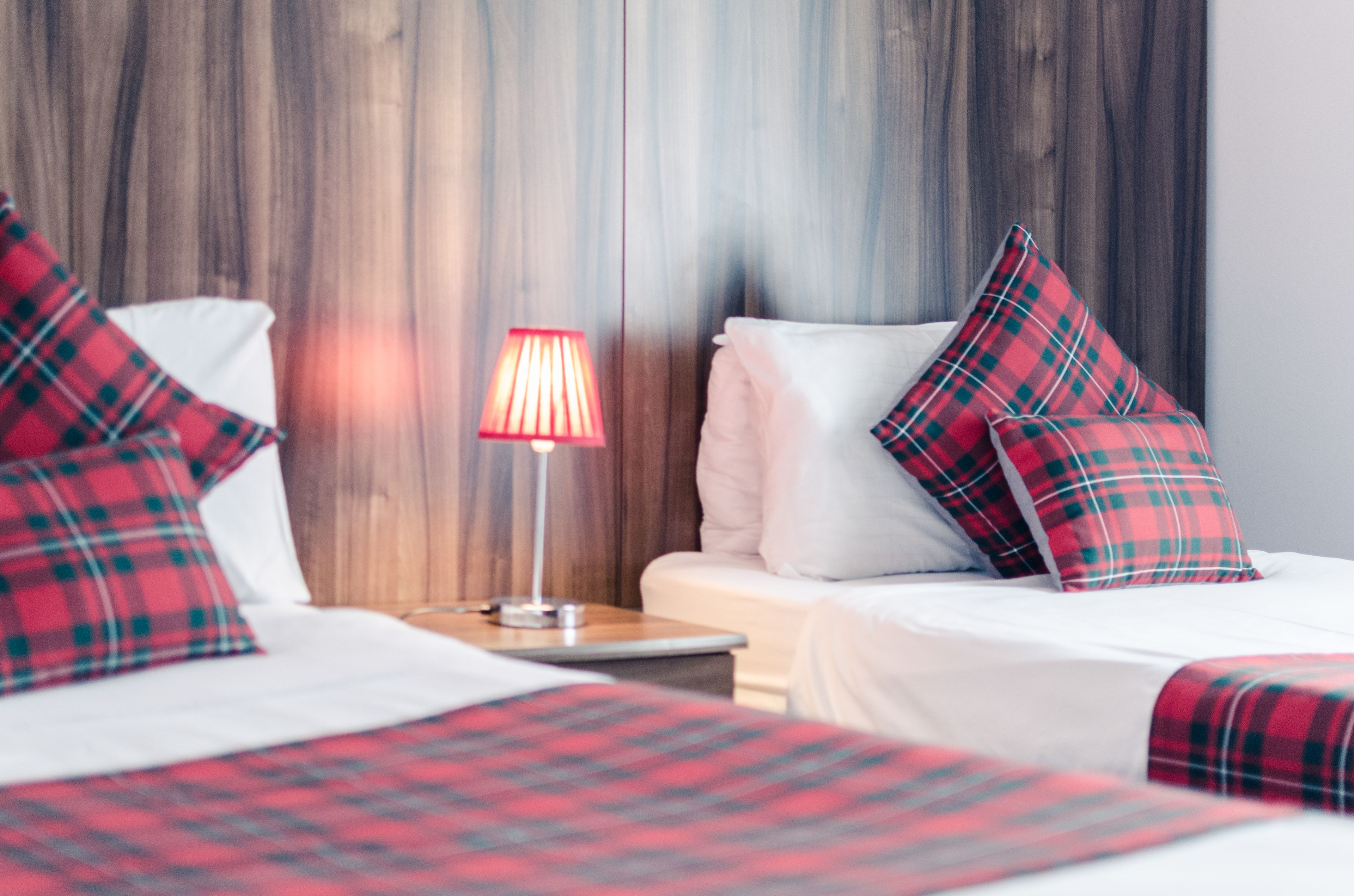 Ett hotellrum med två sängar, rött och grönt rutigt sänglinne, en sänglampa och en sänggavel i trä.