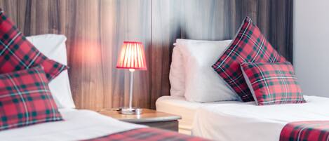 Ett hotellrum med två sängar, rött och grönt rutigt sänglinne, en sänglampa och en sänggavel i trä.