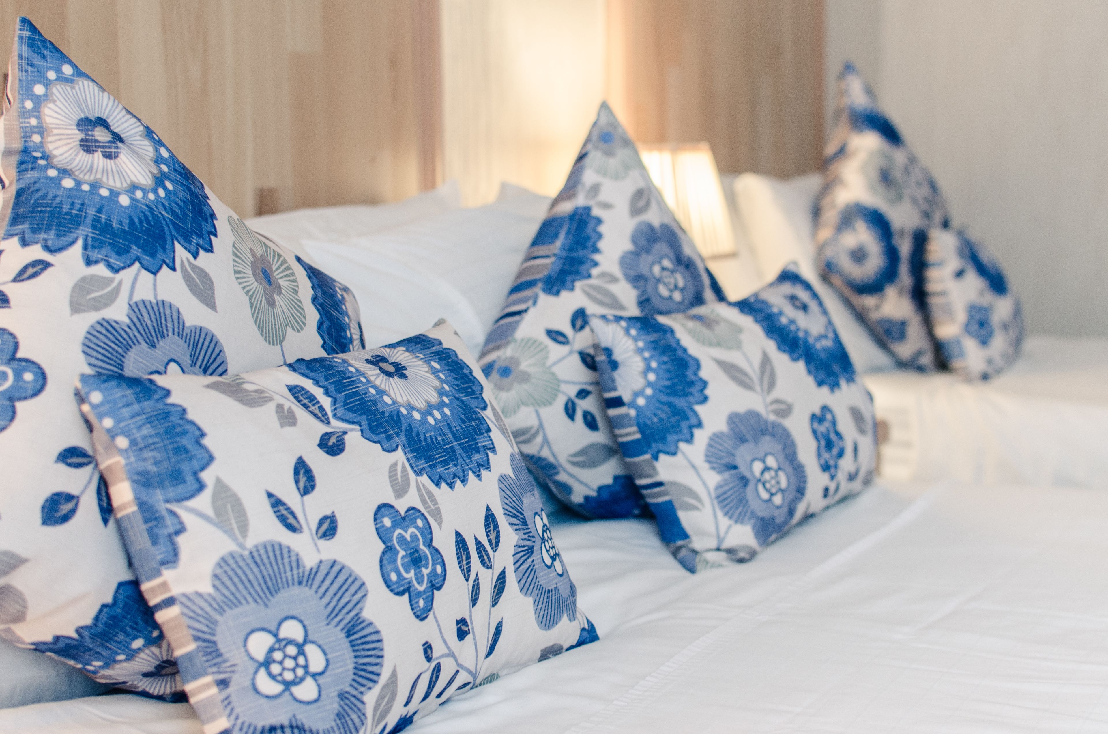 A bed with white bedding and blue floral pillows.