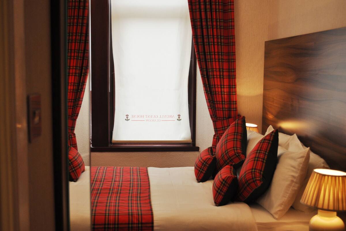 A bed with red plaid bedding, a window with curtains, and a wooden headboard.