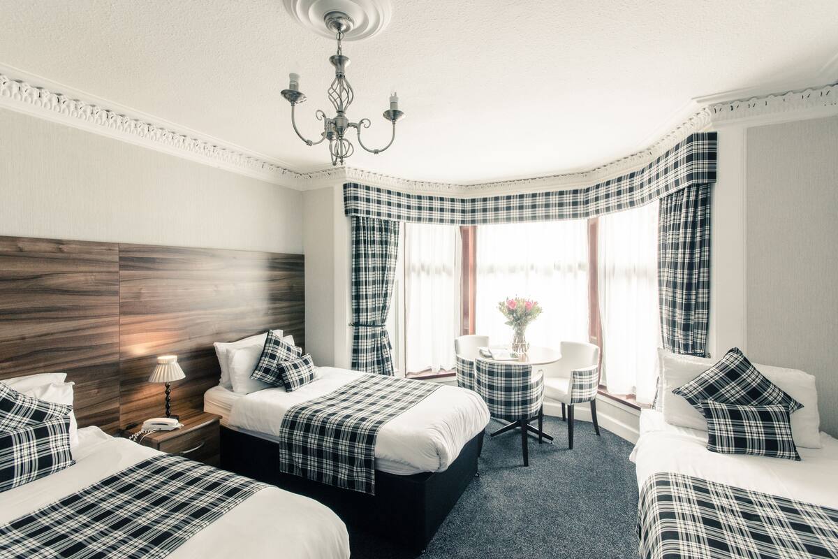 A hotel room with two beds, a chandelier, a round table with chairs, and a window with curtains.