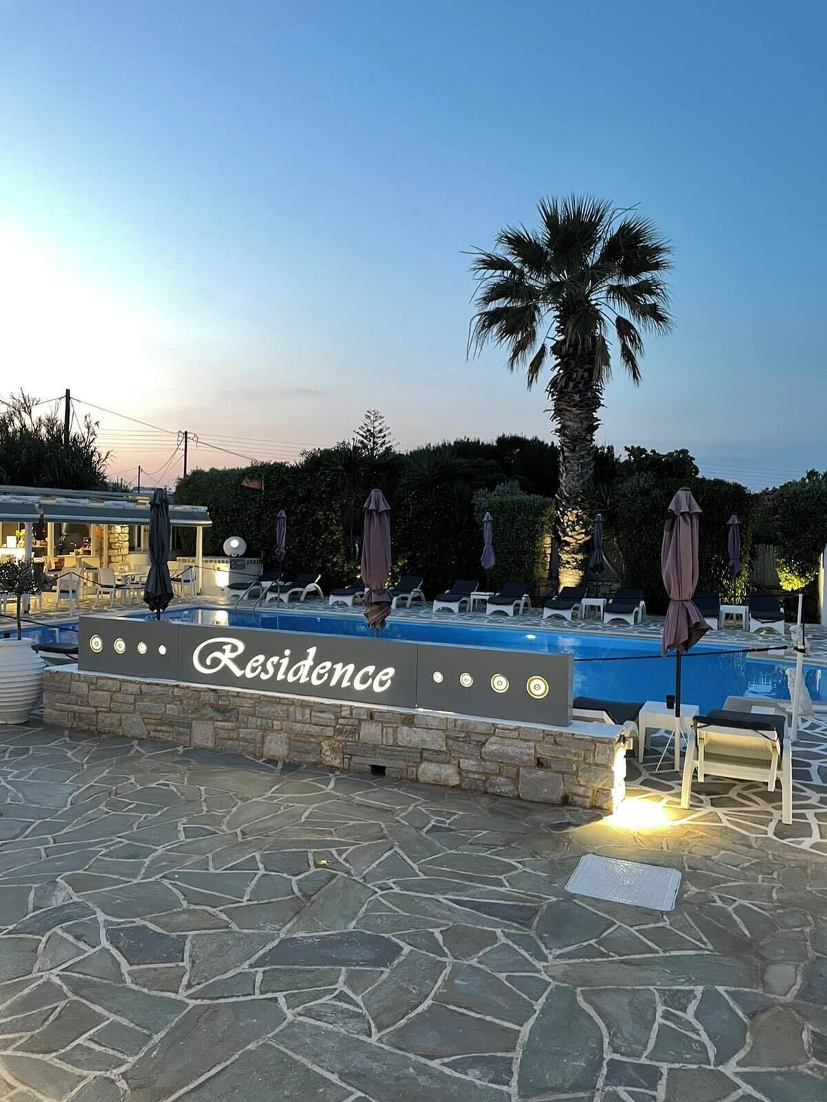 A poolside area with lounge chairs and umbrellas, a sign reading "Residence", and a stone-tiled floor.