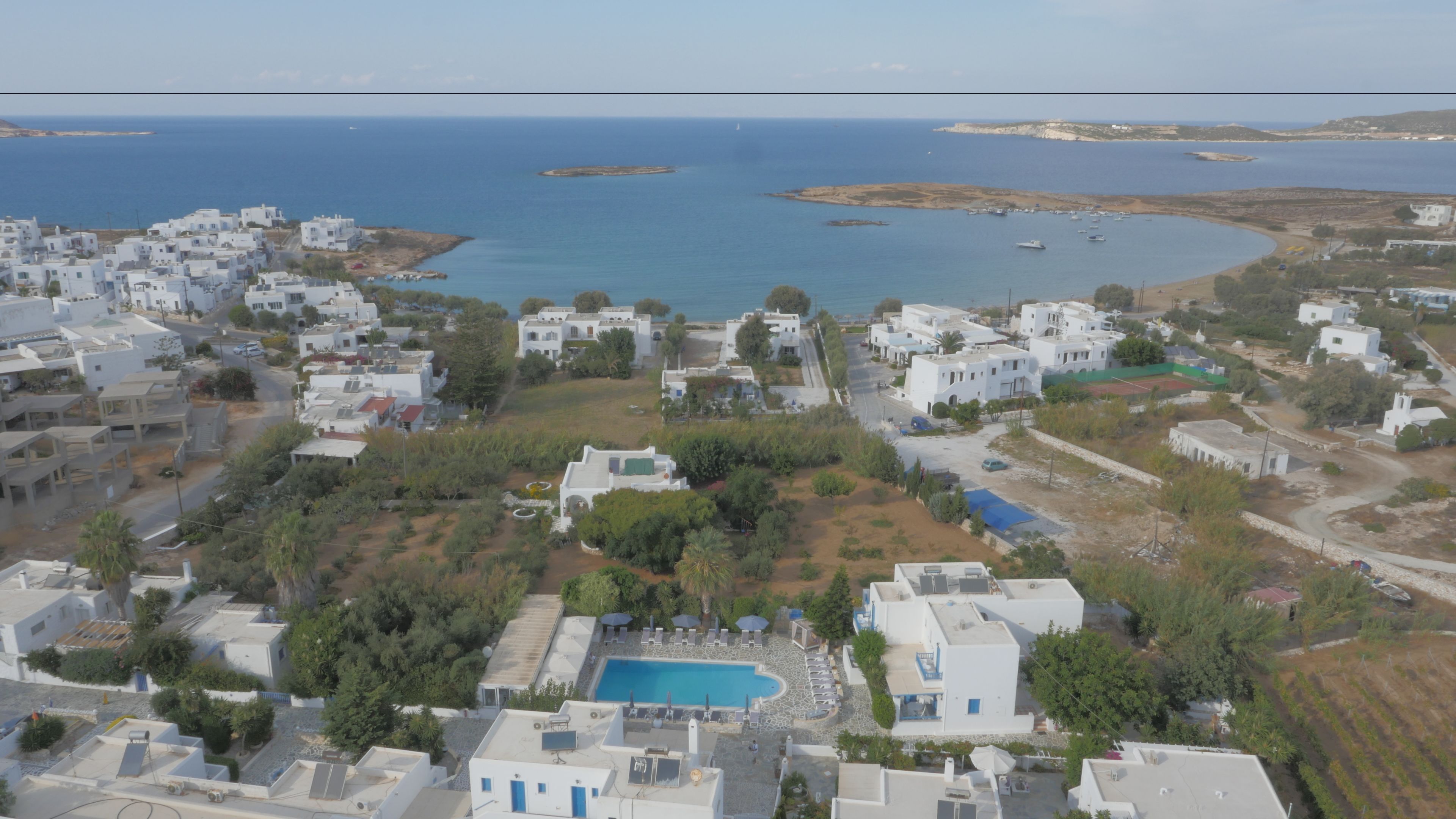 Vista aérea de una zona residencial costera con edificios blancos, una piscina y una vista despejada del mar.