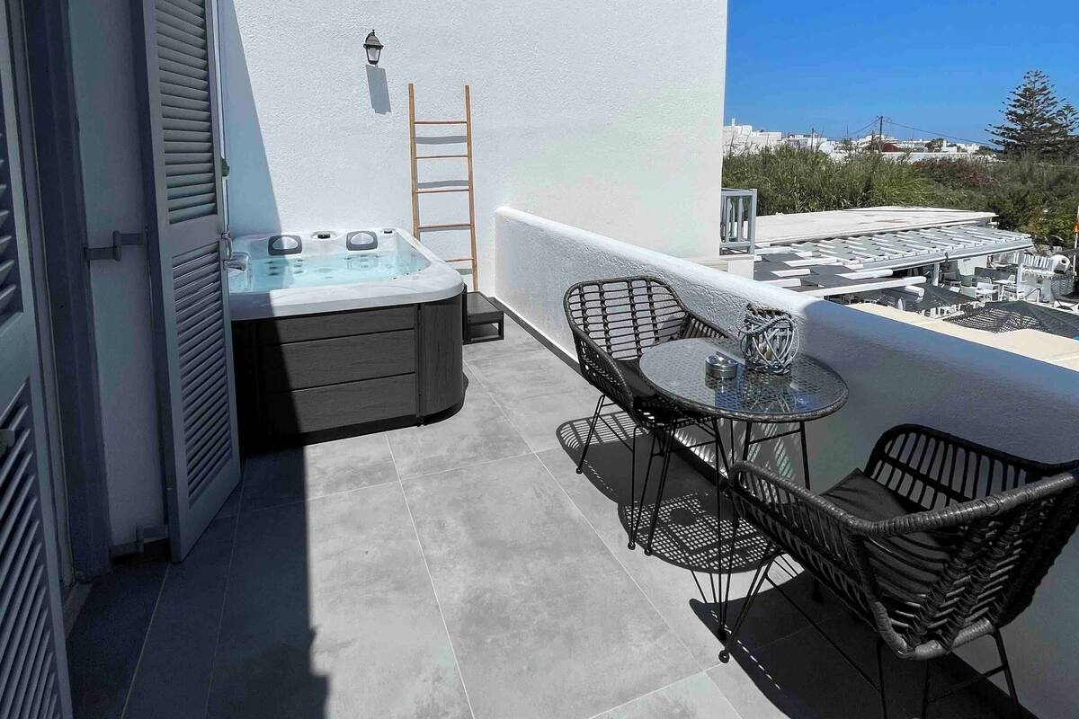 A rooftop terrace with a hot tub, two wicker chairs, a small table, and a ladder.