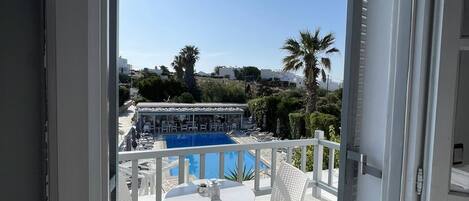 A balcony with a white table and chairs, overlooking a pool area with lounge chairs and a clear blue sky.