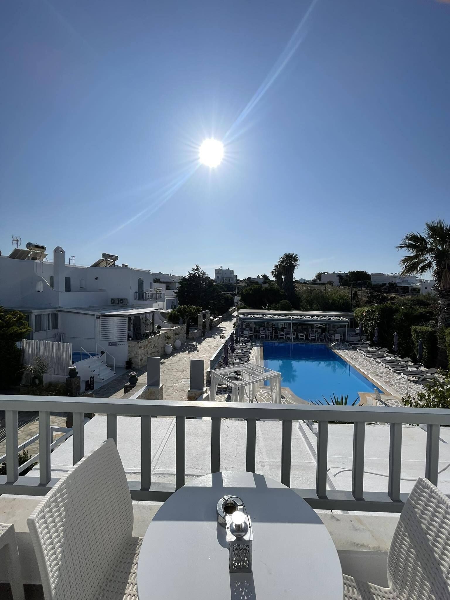 A poolside view with a clear sky, a sunlit pool, and modern buildings in the background.