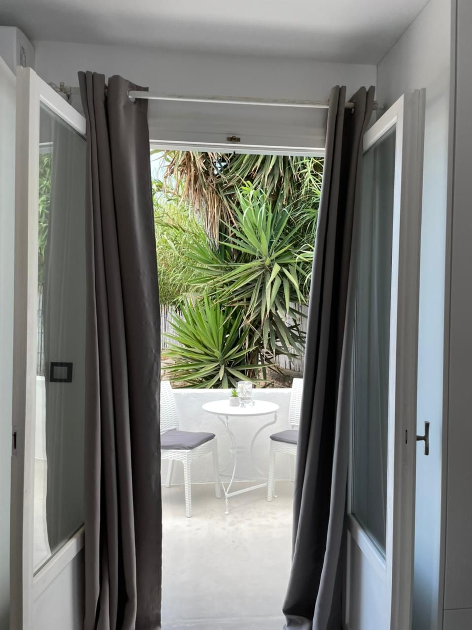 Une porte-fenêtre donnant sur un patio extérieur aménagé avec une table et des chaises, le tout entouré de verdure.
