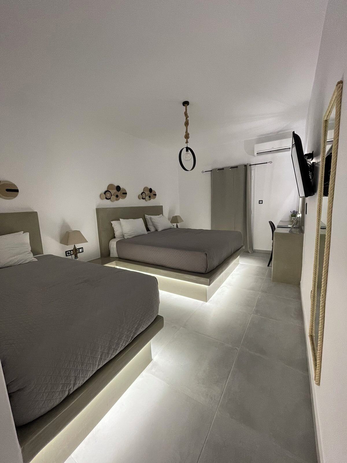A modern bedroom with two beds, a TV, and a ceiling light.
