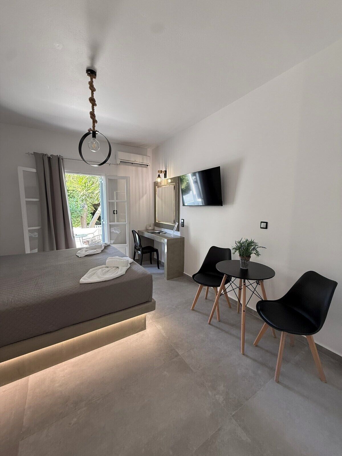 A modern bedroom with a bed, desk, chairs, and a TV.
