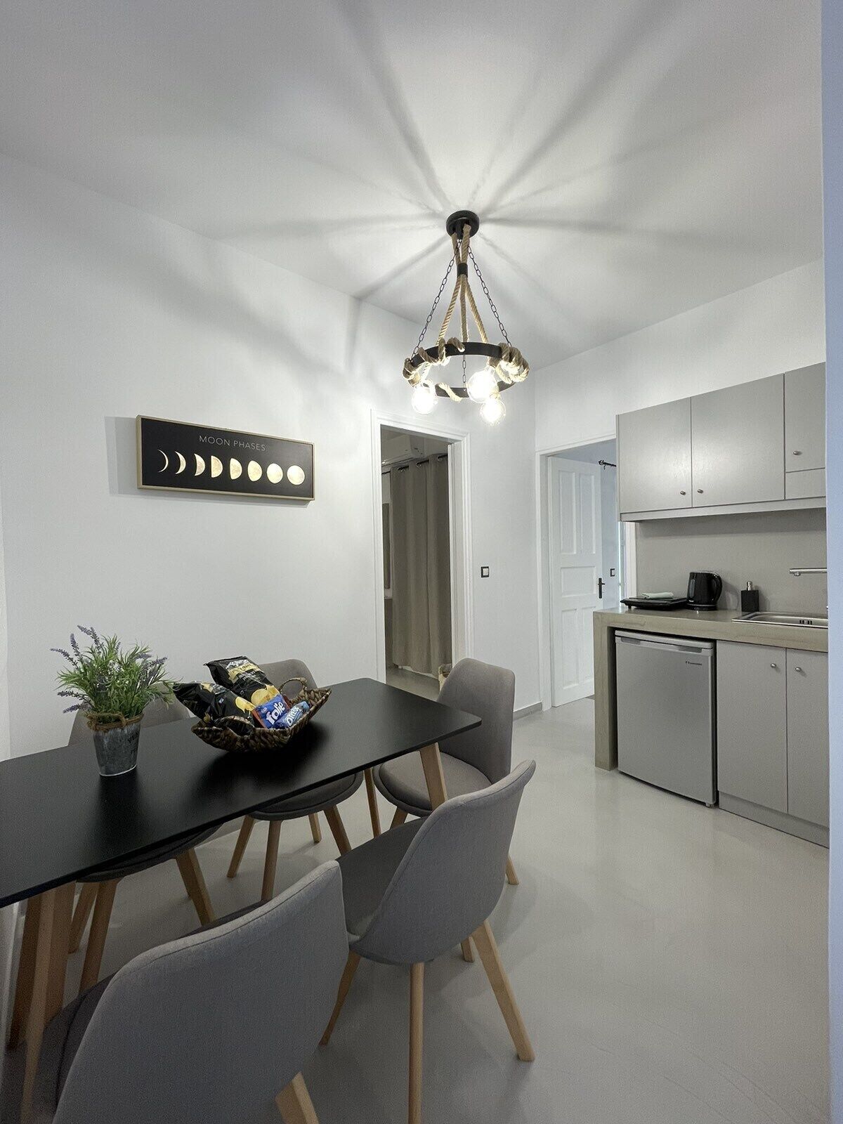 A modern kitchen with grey cabinets, a black dining table with grey chairs, a chandelier, and a wall-mounted sign displaying moon phases.