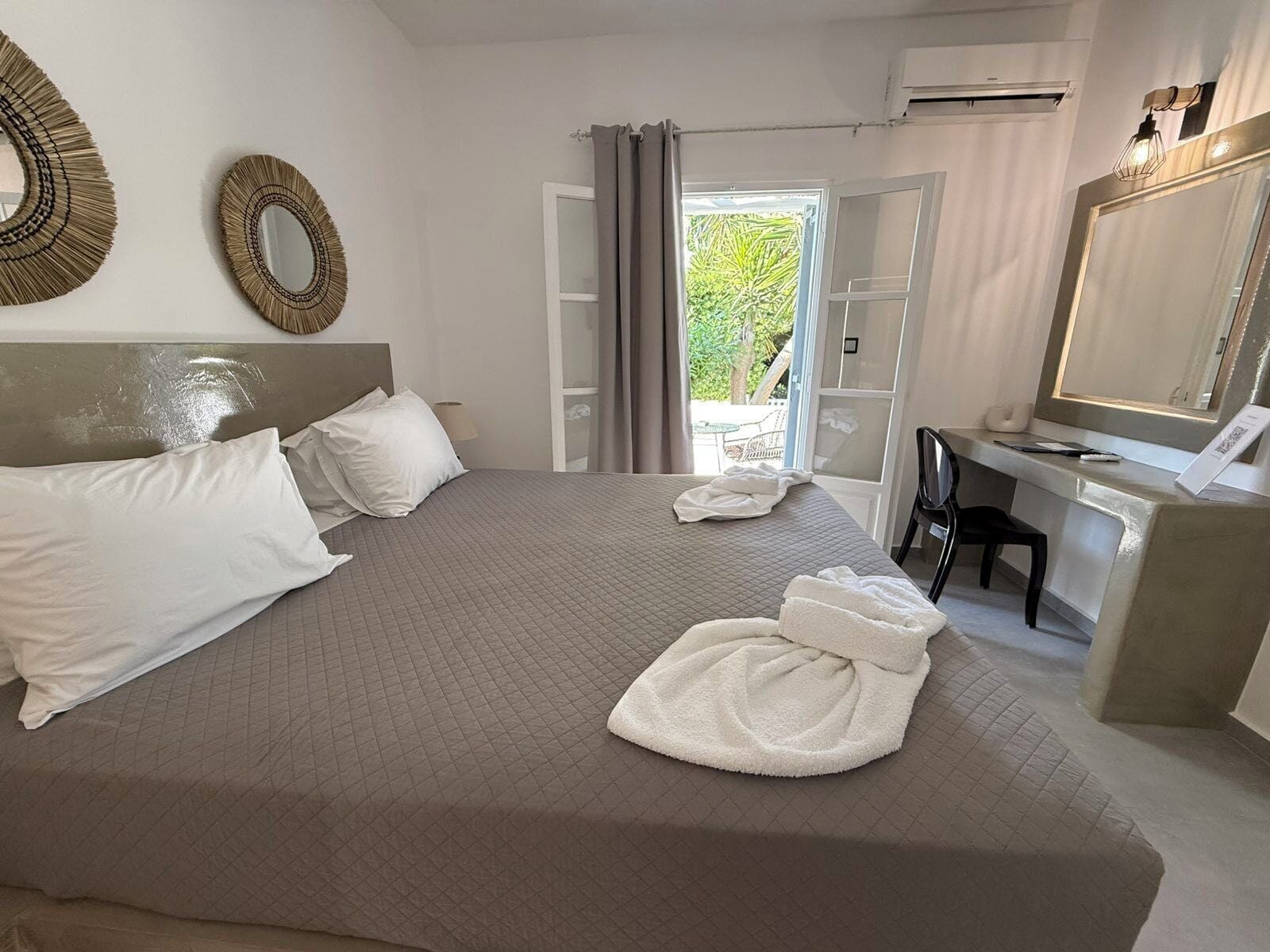 Une chambre d’hôtel équipée d’un lit, d’un bureau, d’une chaise, d’un miroir et offrant une vue sur la verdure environnante.