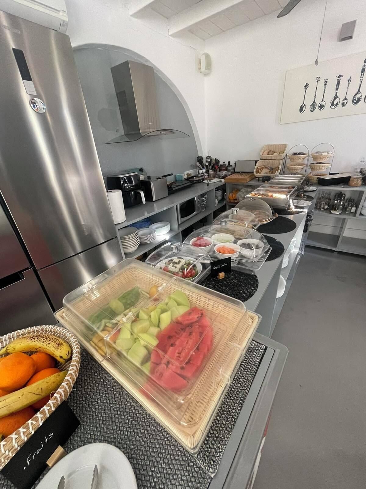 A buffet setup with various food items, including fruits and salads, in a modern kitchen setting.