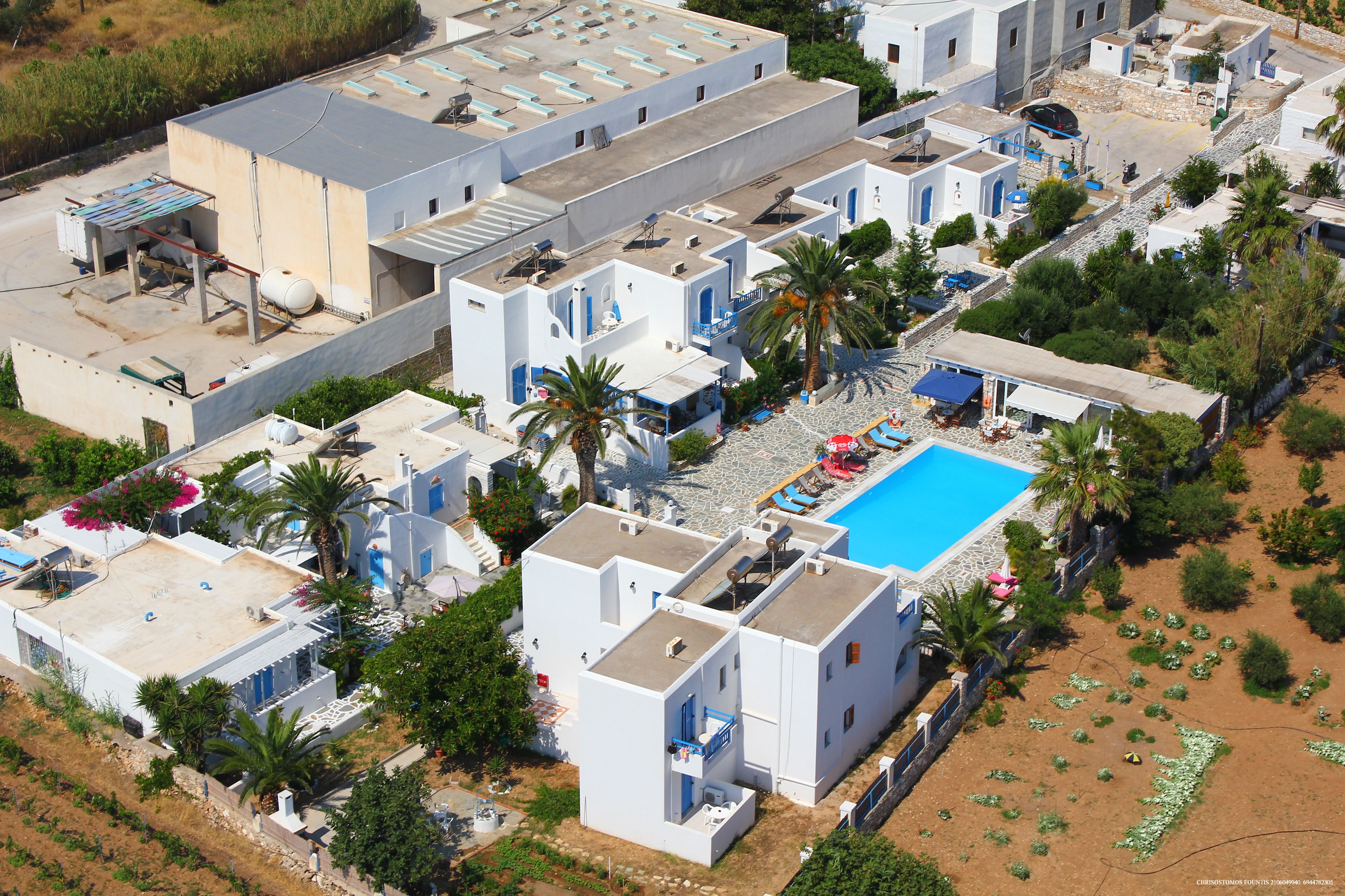 An aerial view of a residential area with multiple white buildings, a swimming pool, and surrounding greenery.