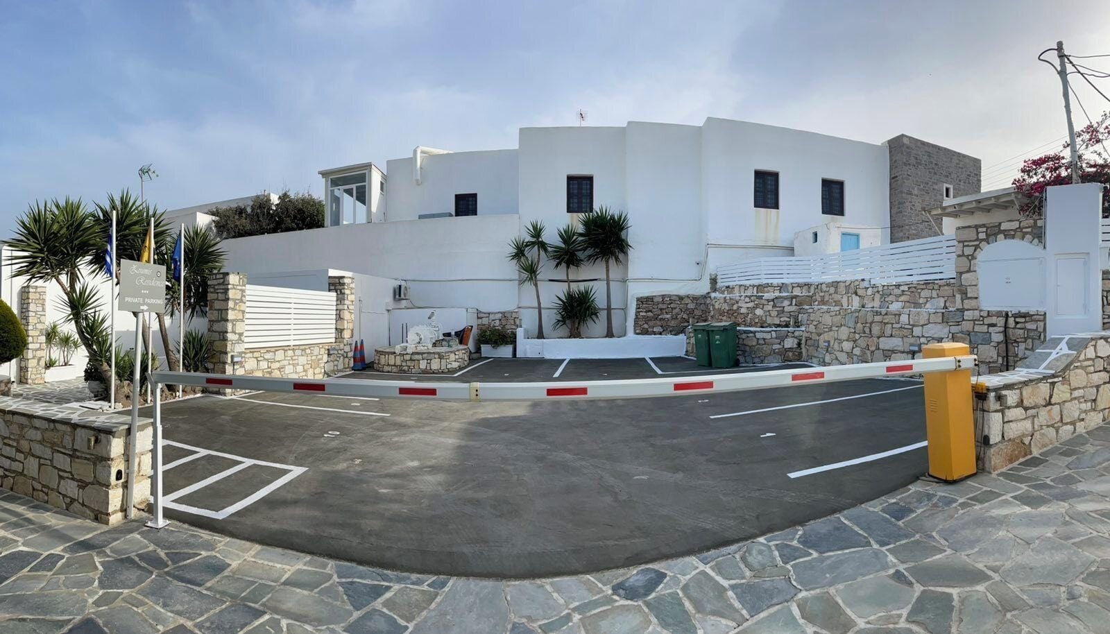 A gated parking area with a stone wall and a white building in the background.