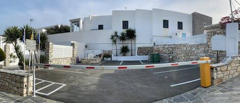 A gated parking area with a stone wall and a white building in the background.
