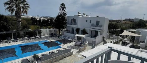 A pool area with lounge chairs, a table with a decorative item, and a view of a white building with a balcony.