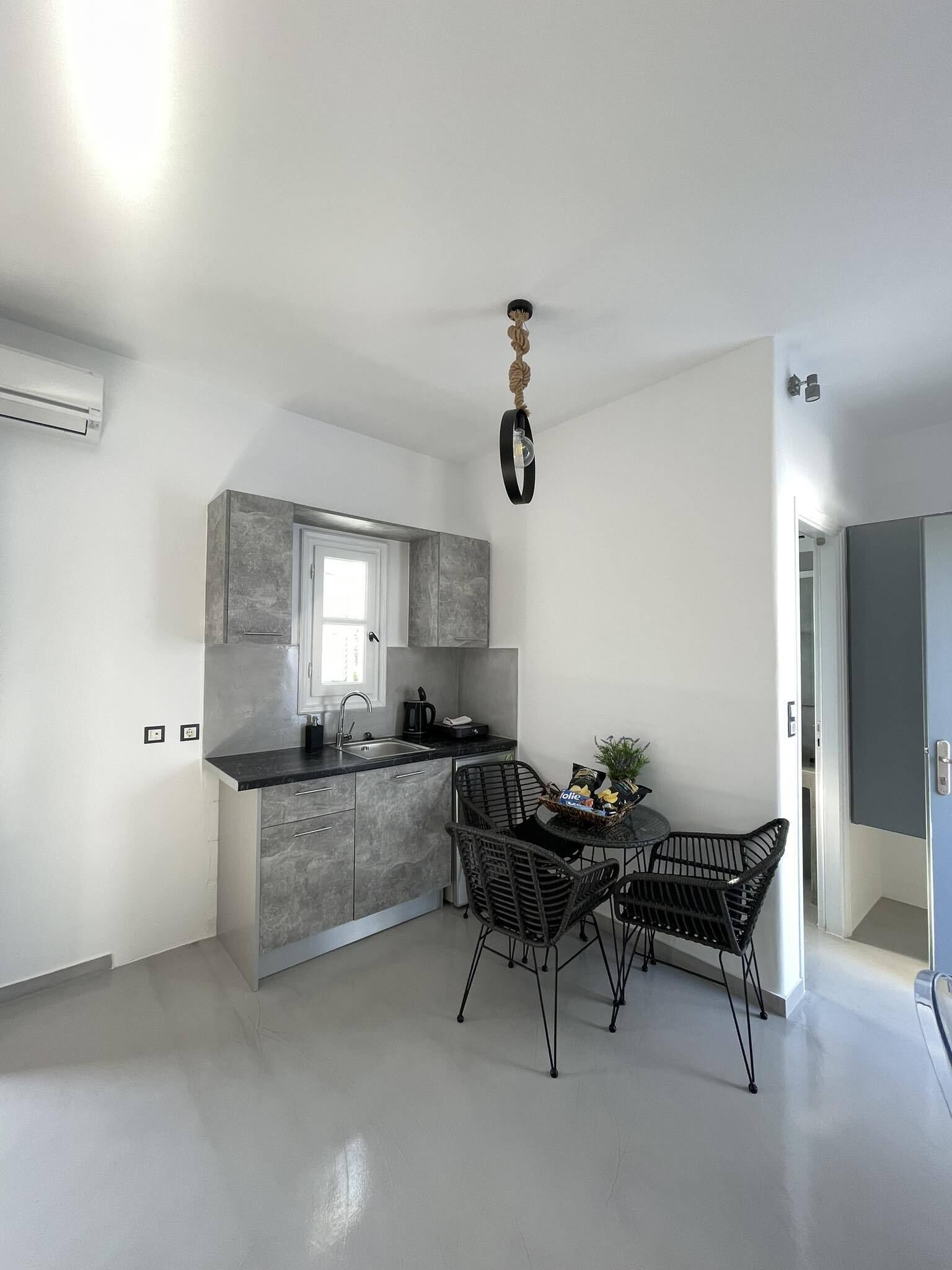 A modern kitchen with grey cabinetry, a window, and a dining area with wicker chairs.