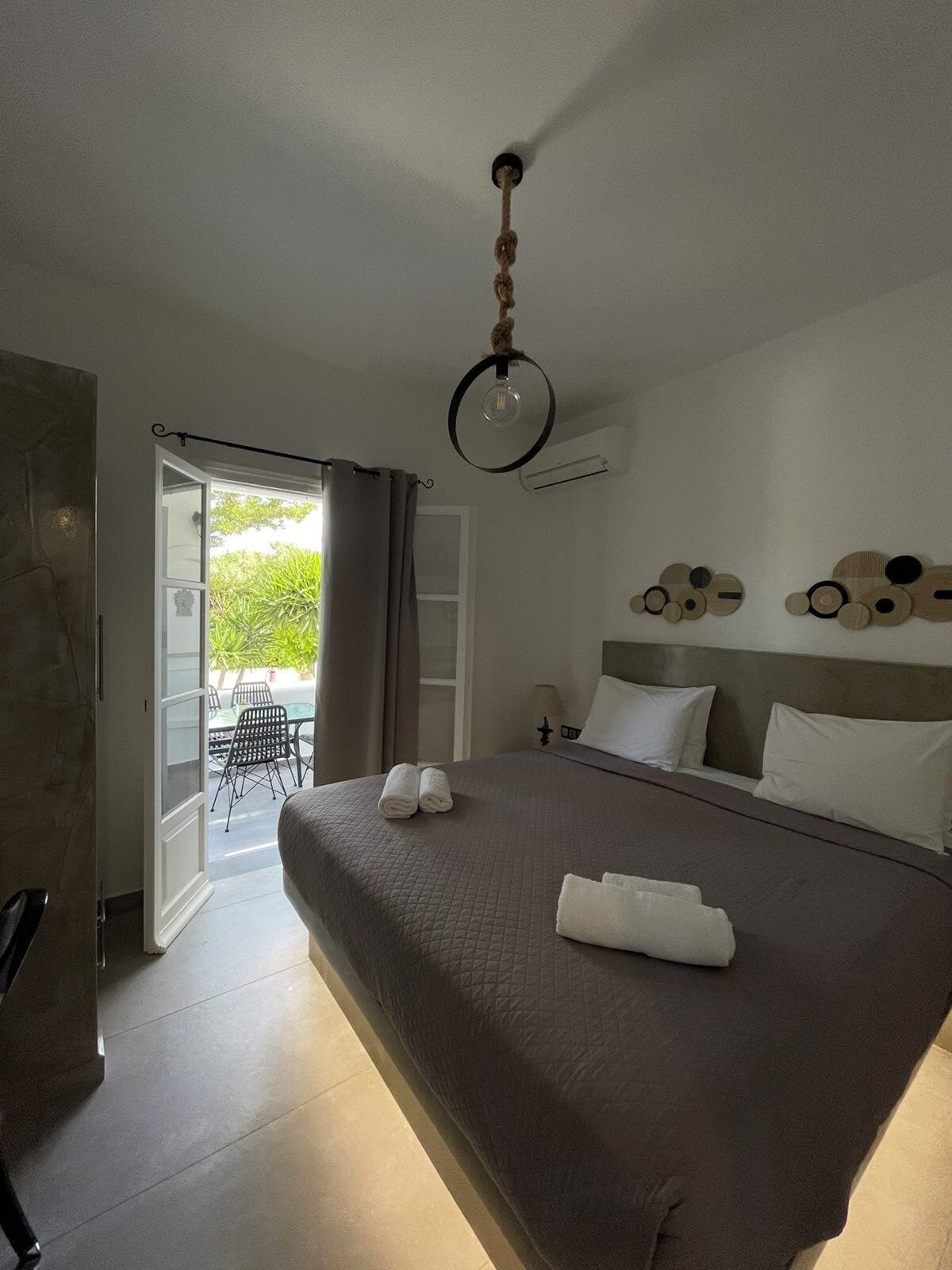 A hotel room with a bed, a ceiling light, a view of the outdoors, and a door leading to a balcony.