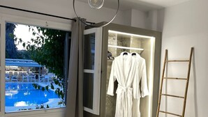 A hotel room with a bed, a robe, a towel, a ladder, and a view of a pool.