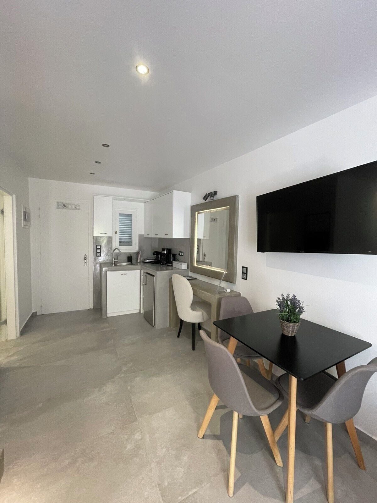 A modern kitchen with white cabinets, a coffee machine, and a dining area with a black table and grey chairs.