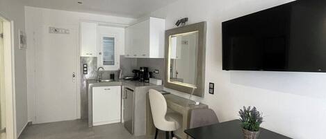 A modern kitchen with white cabinets, a coffee machine, and a dining area with a black table and grey chairs.