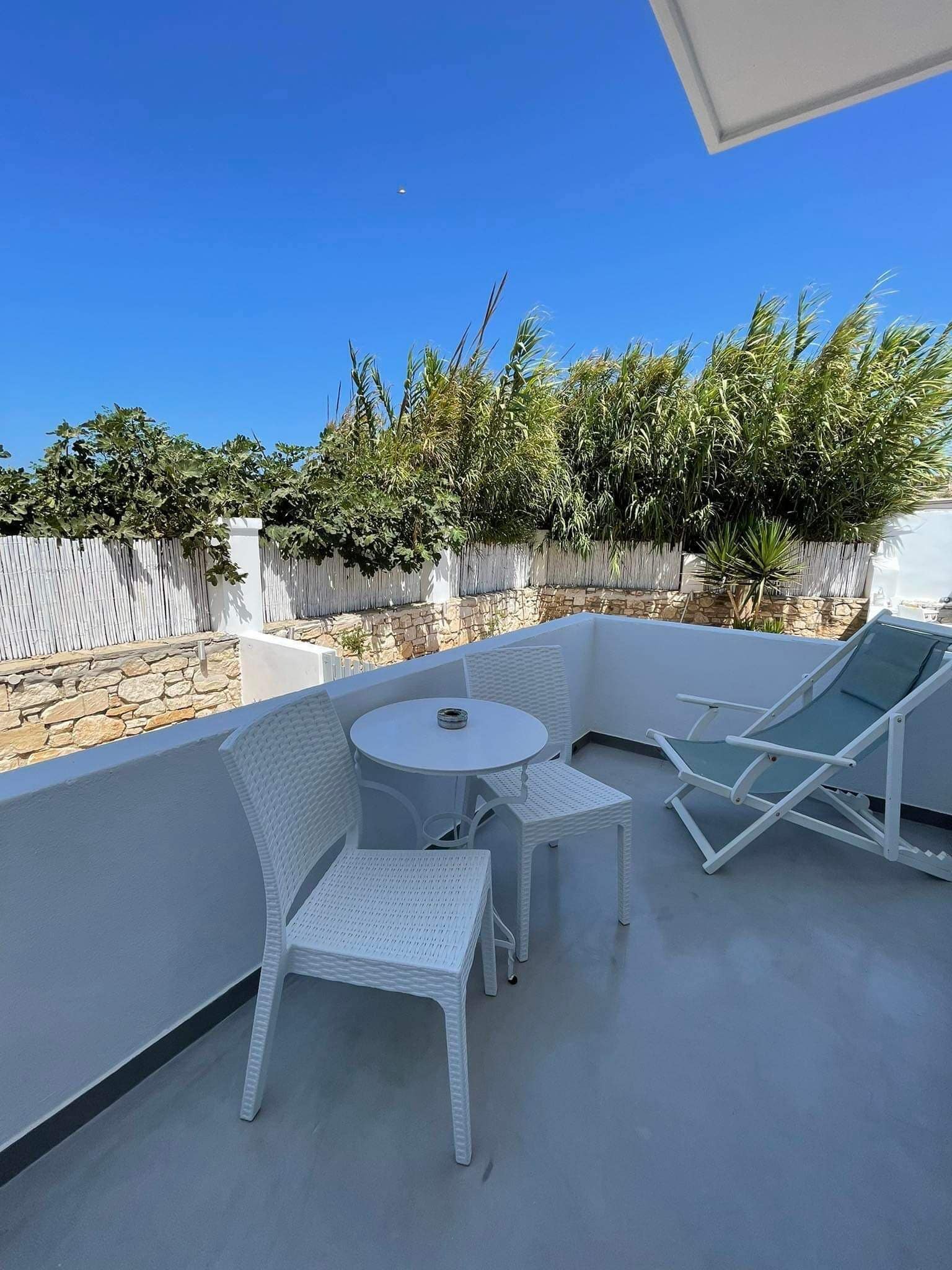 Un balcone con mobili in vimini bianco, un muro in pietra e vista sul verde.