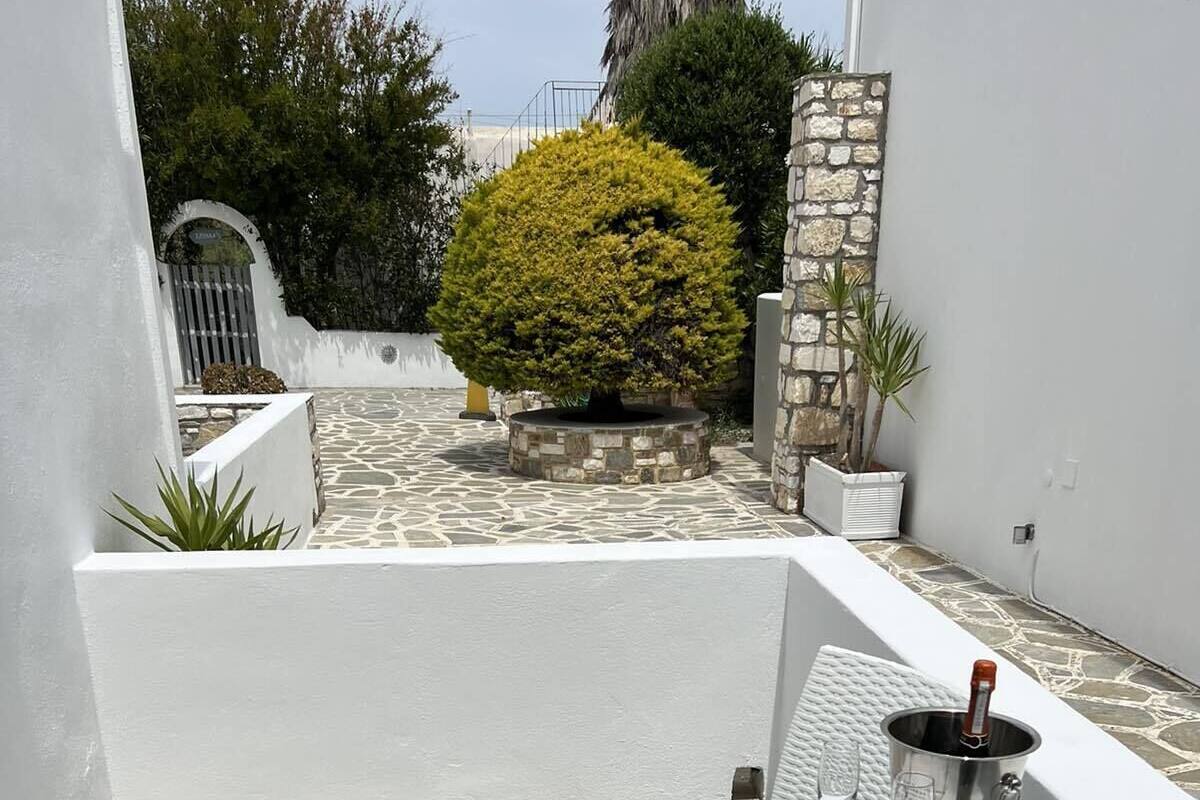 A small outdoor patio with a round table and two chairs, a potted plant, and a bottle of champagne.