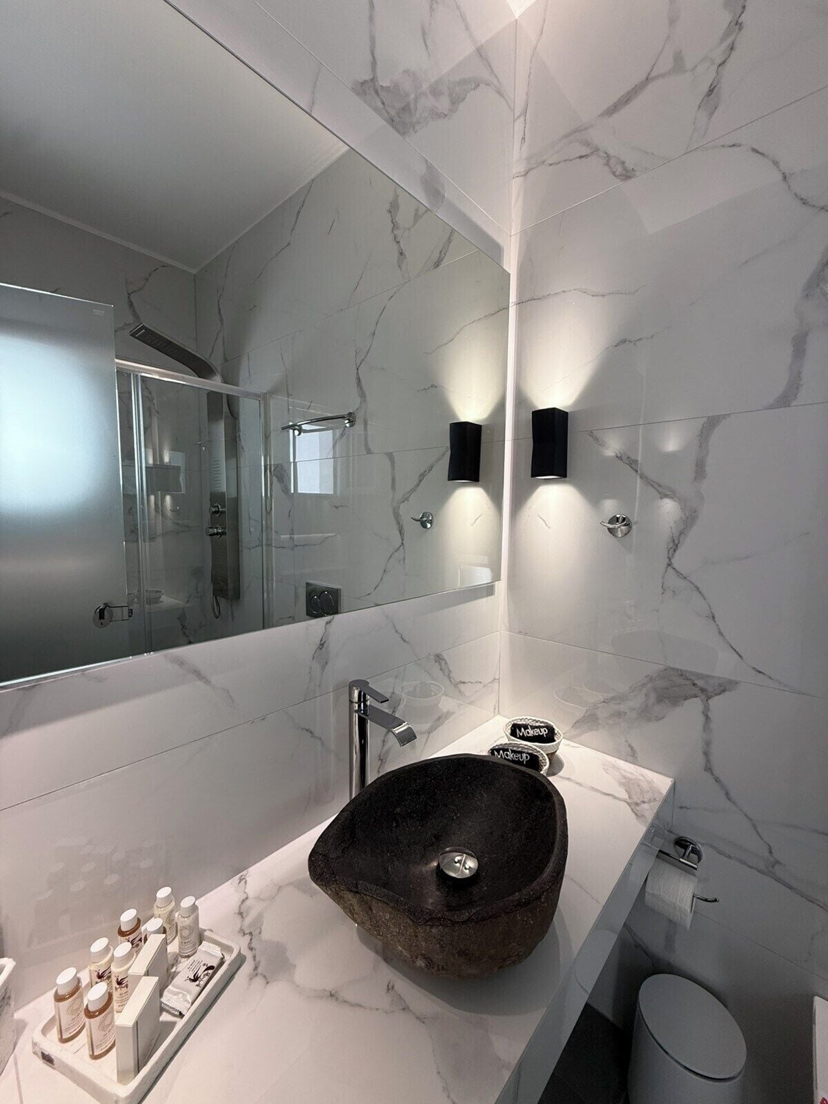 Une salle de bain moderne avec un grand miroir, des murs en marbre, un lavabo en pierre et une douche à parois de verre.