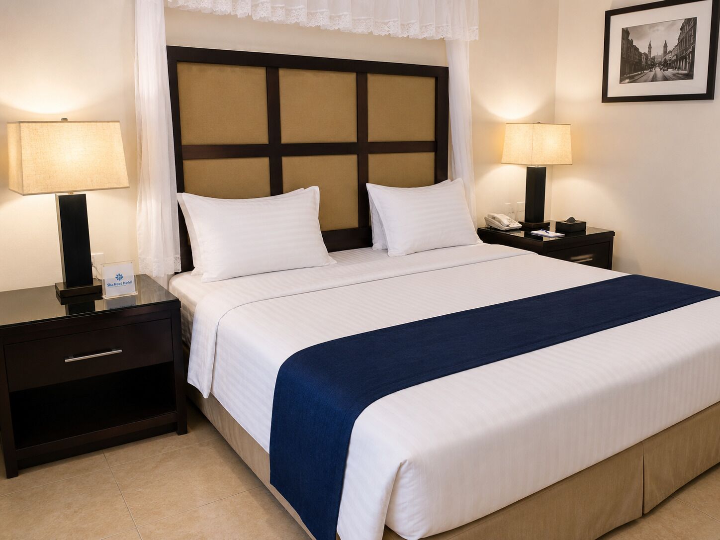 Une chambre d’hôtel avec un lit, deux tables de chevet, une commode, une lampe, un téléphone et un tableau encadré au mur.