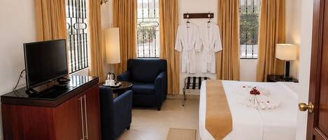 A hotel room with a bed, a desk with a TV, a chair, a ceiling fan, and a window with curtains.