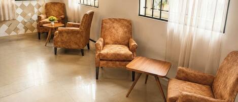 A room with four patterned armchairs, a small wooden table, and large windows with curtains.