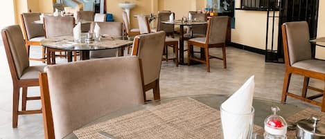 A hotel dining area with multiple tables and chairs, a fire extinguisher, a television, and a view of the outside.