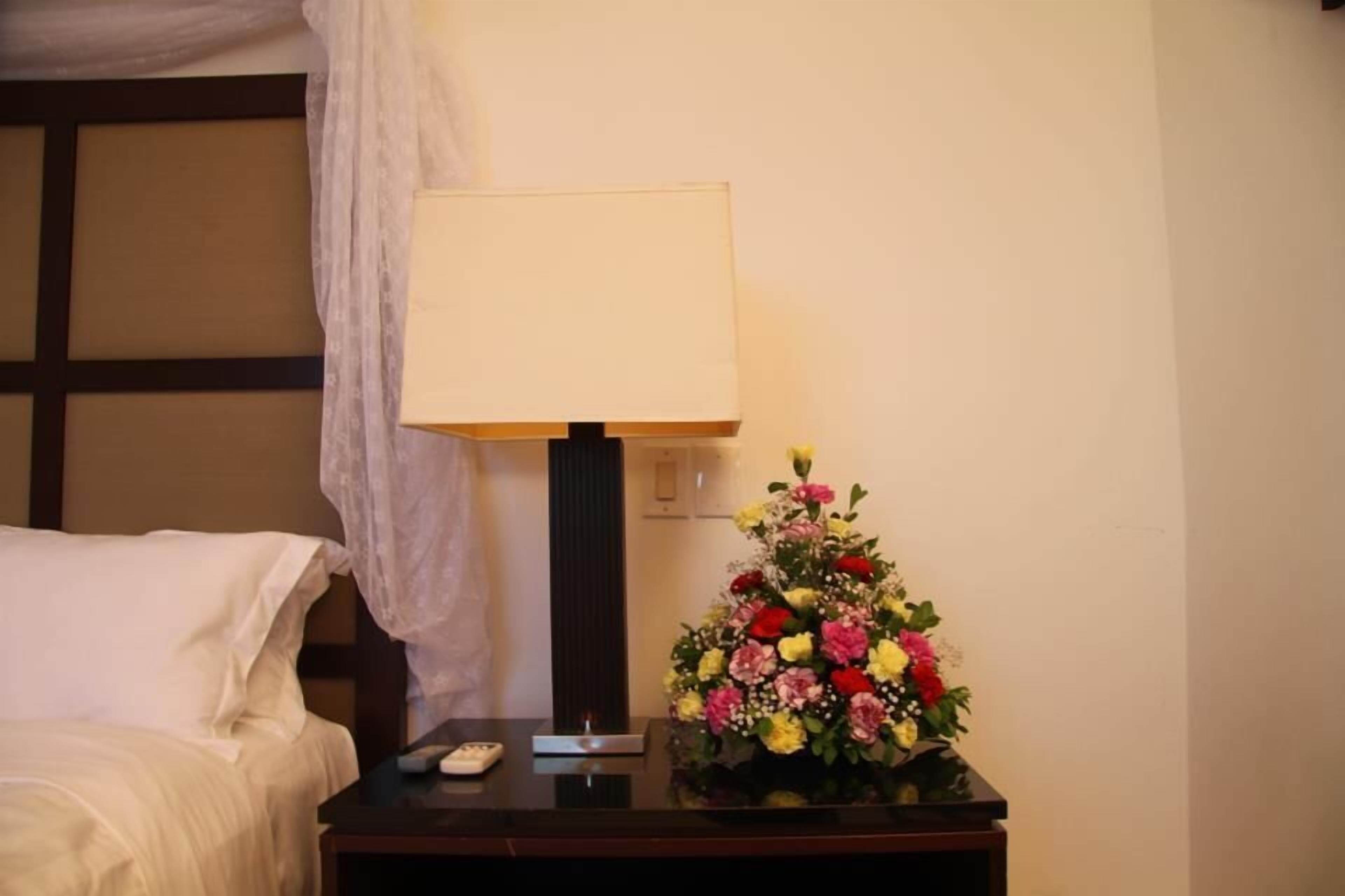 Una habitación de hotel con una cama, una mesita de noche con una lámpara y un arreglo floral.